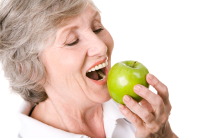 older woman with dental implants eating an apple